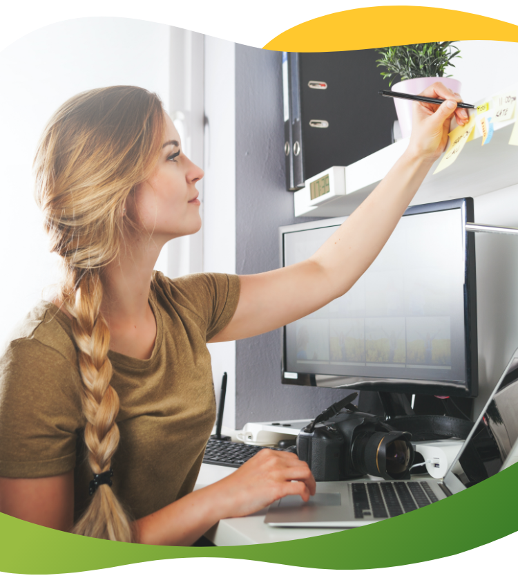 A young woman with blonde braided pigtail sits at her desk making notes on her post it